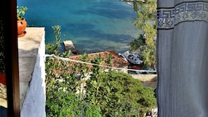 A coastal view with a boat on the water, a building with a red roof, and greenery. - Arbeli House for idyllic sun & sea holidays in Mandraki Bay, Hydra (Idra)