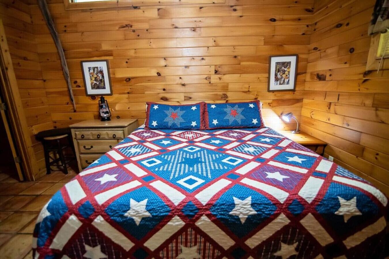 Une pièce de style cabane en bois, avec un lit, une table de chevet, une commode et deux tableaux encadrés accrochés aux murs.
