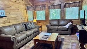 Interior d'una cabana de fusta amb dos sofàs de pell, una taula de centre de fusta i una llar de foc.