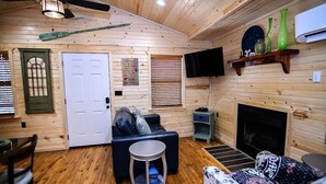 Interior acogedor de una cabaña con piso de madera, un sofá, una mesita redonda, un televisor y una chimenea.