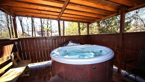 Una terraza de madera con un jacuzzi, bancos de madera y un área cubierta.