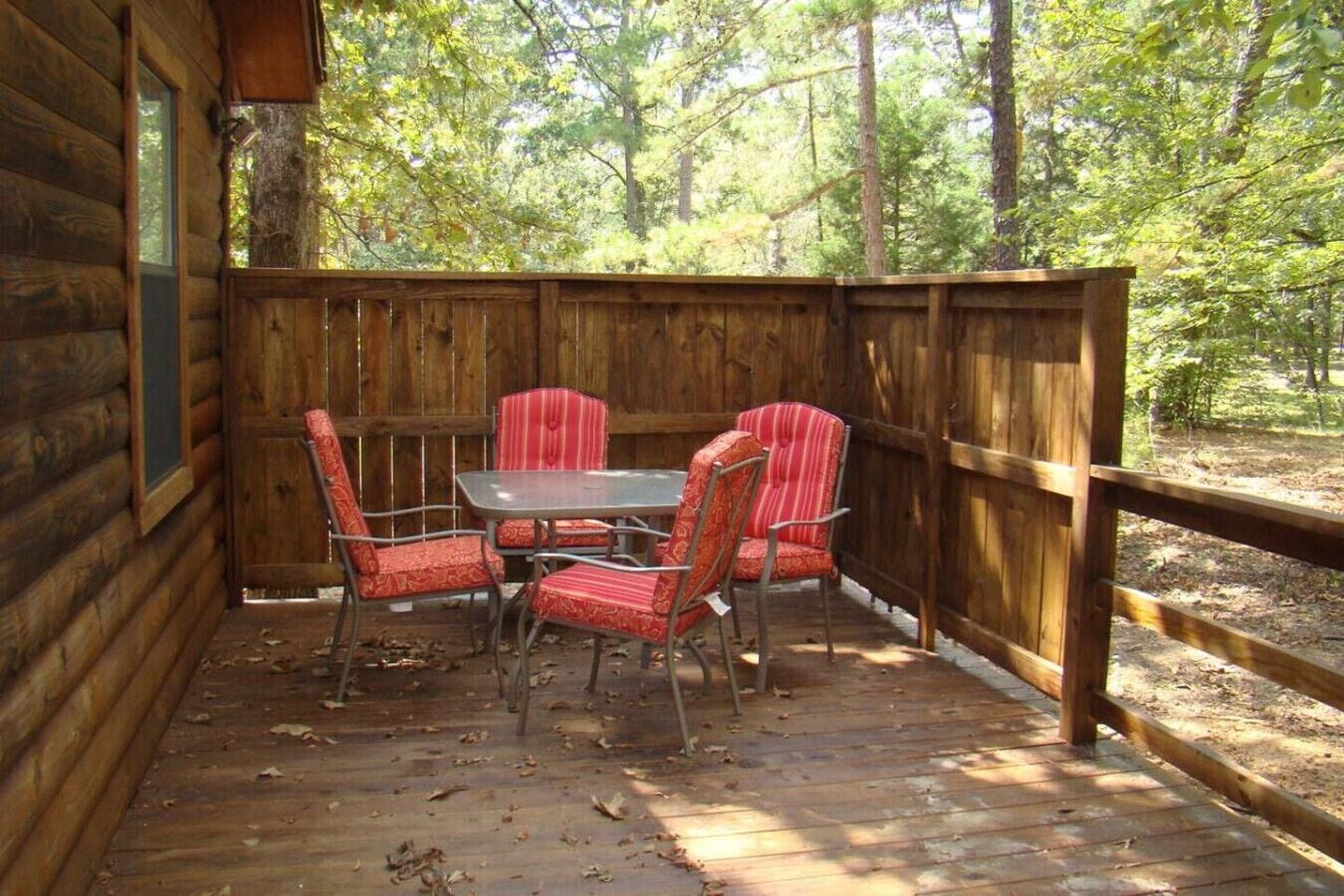 Eine Holzterrasse mit Tisch und vier gestreiften Stühlen, umgeben von einem Holzzaun und Bäumen.