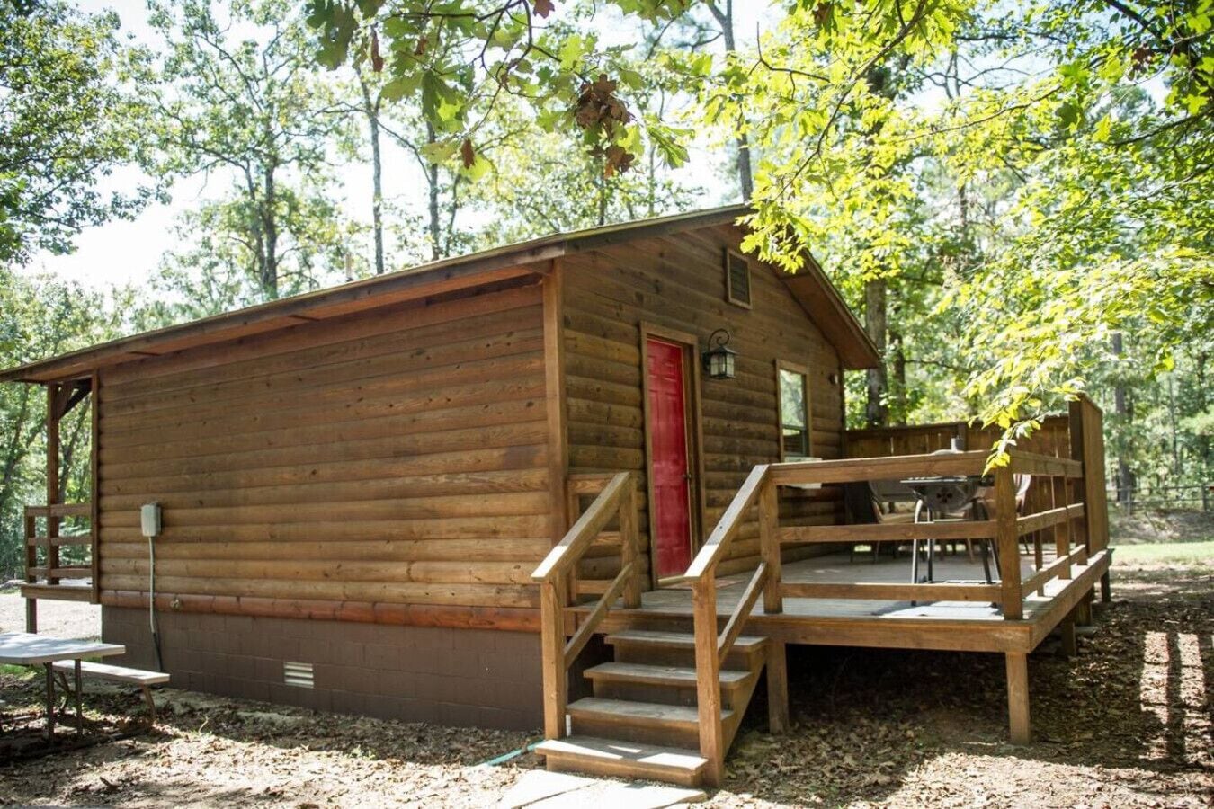 Une cabane en bois avec une porte rouge, une véranda et une table de pique-nique.