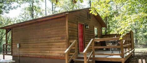 A wooden cabin with a red door, a porch, and a picnic table.