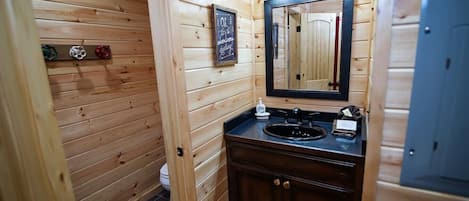 Une salle de bain rustique, aménagée dans une cabane en bois, avec un lavabo, un miroir et un panneau encadré accroché au mur.
