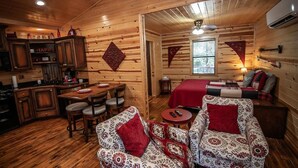 A cozy cabin interior with a dining area, kitchen, and a bed with a red blanket. - Cozy Hochatown Cabin w/ Private Hot Tub (Broken Bow)