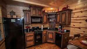 A compact kitchen with wooden cabinets, a refrigerator, stove, microwave, and a coffee maker. - Cozy Hochatown Cabin w/ Private Hot Tub (Broken Bow)