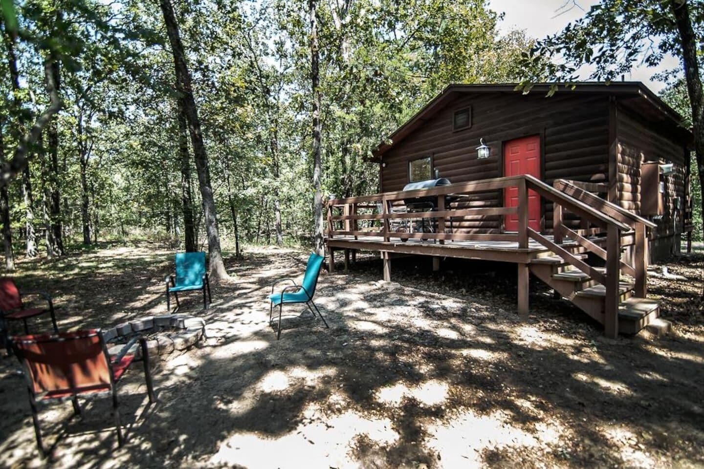 Un chalet rustique avec une terrasse en bois et une porte rouge, entouré d’arbres.