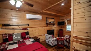 A cozy cabin room with a bed, a fireplace, a TV, and a small table with chairs. - Cozy Hochatown Cabin w/ Private Hot Tub (Broken Bow)