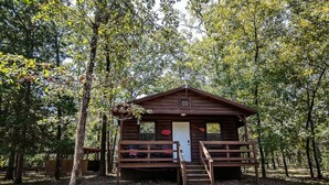 A wooden cabin with a porch, surrounded by trees. - Cozy Hochatown Cabin w/ Private Hot Tub (Broken Bow)