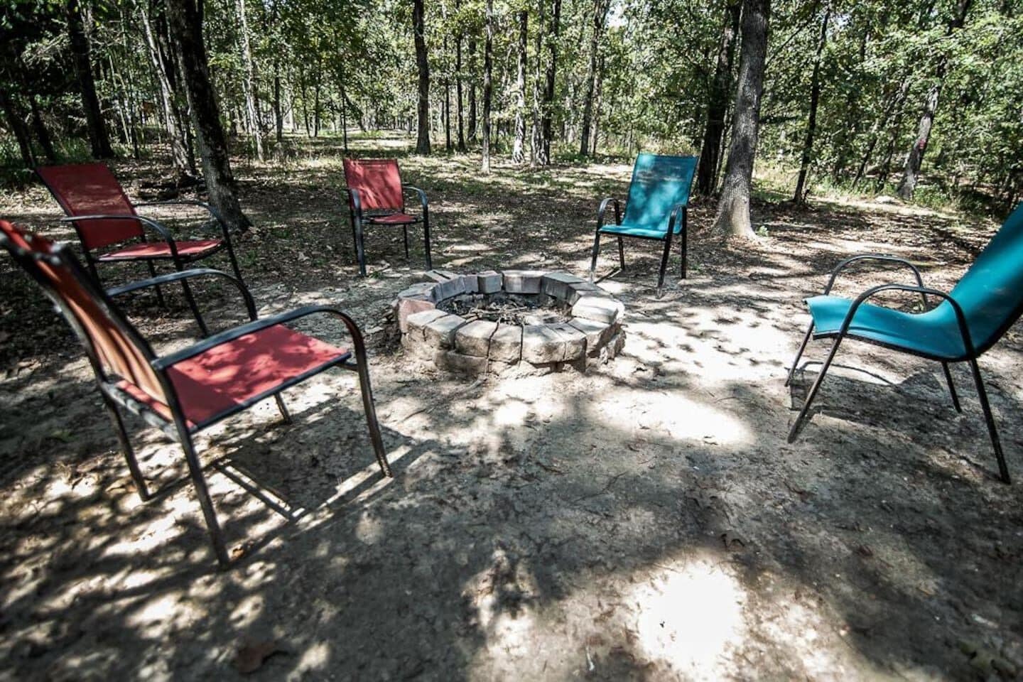 A circular stone fire pit surrounded by four chairs in a forested area.