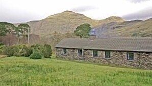A stone house with a sloped roof, surrounded by green fields and a mountain in the background. - The perfect place to take a step back from it all (Renvyle)