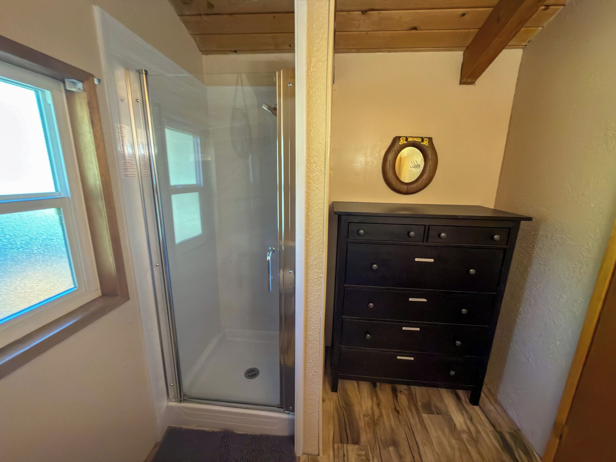 Un baño con cabina de ducha de vidrio, techo de madera, cómoda negra con cajones y un espejo en la pared.