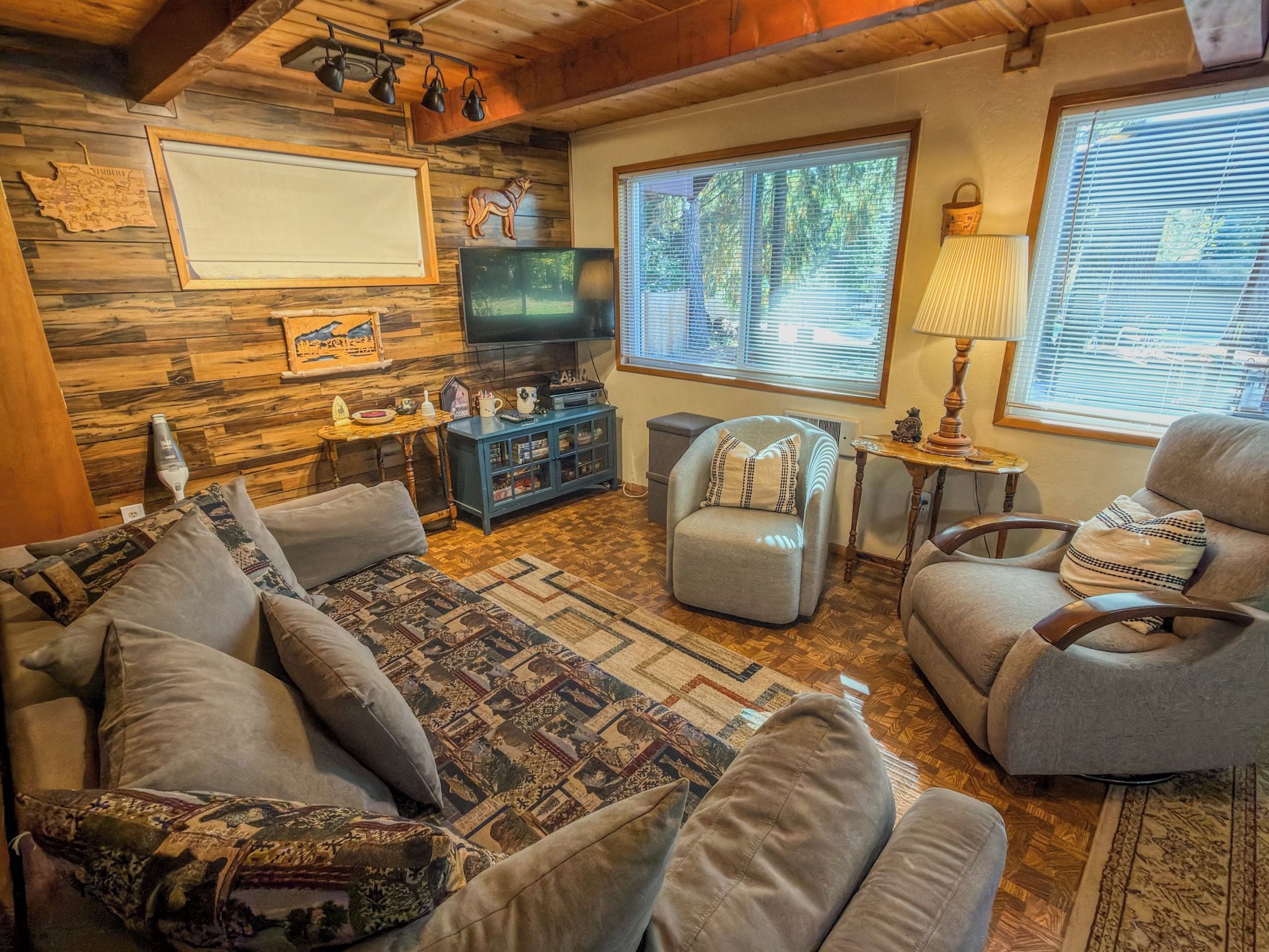 A cozy living room with a sofa, armchairs, a television, and a wooden wall.