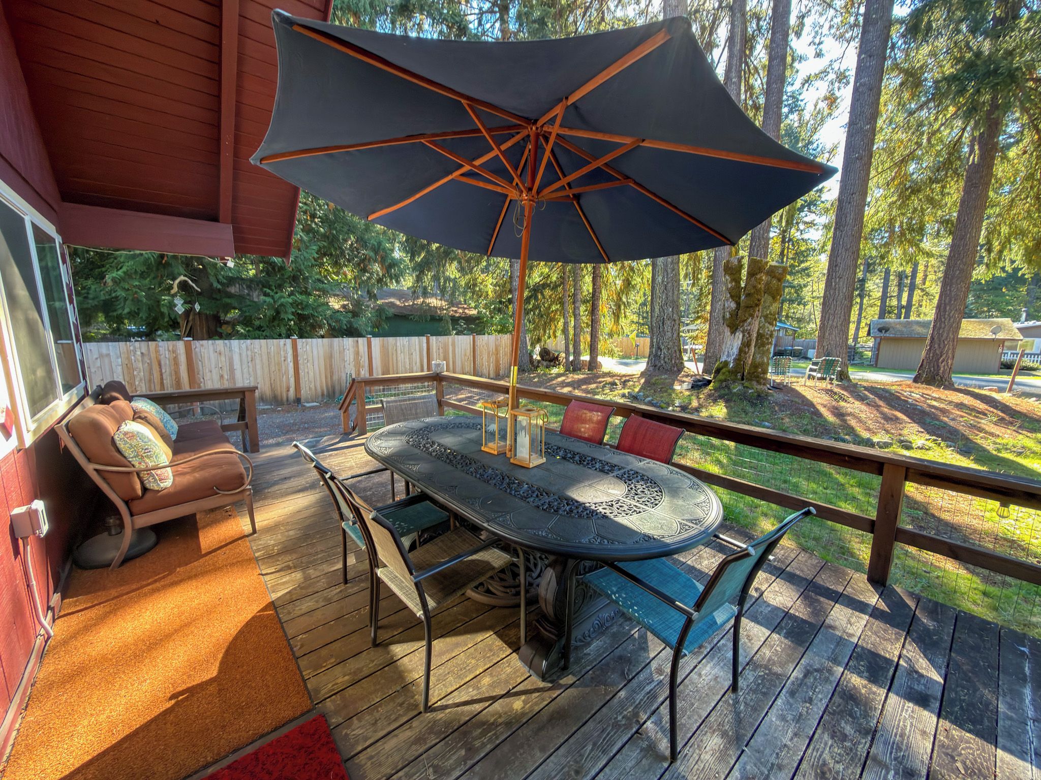 An outdoor deck with a table and chairs, a large umbrella, and a wooden fence.