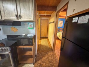 A narrow kitchen with wooden cabinets, a stove, a microwave, and a refrigerator.