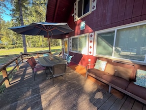 A covered outdoor deck with a table and chairs, a sofa, and a large umbrella.