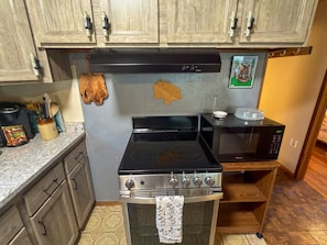 A kitchen with wooden cabinets, a black stove, a microwave, and a small shelf with a picture frame. - Papa`s Packwood Cabin (Packwood)