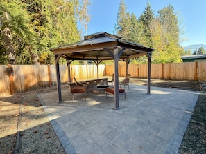 An outdoor patio with a covered seating area, stone flooring, and a wooden fence in the background. - Papa`s Packwood Cabin (Packwood)