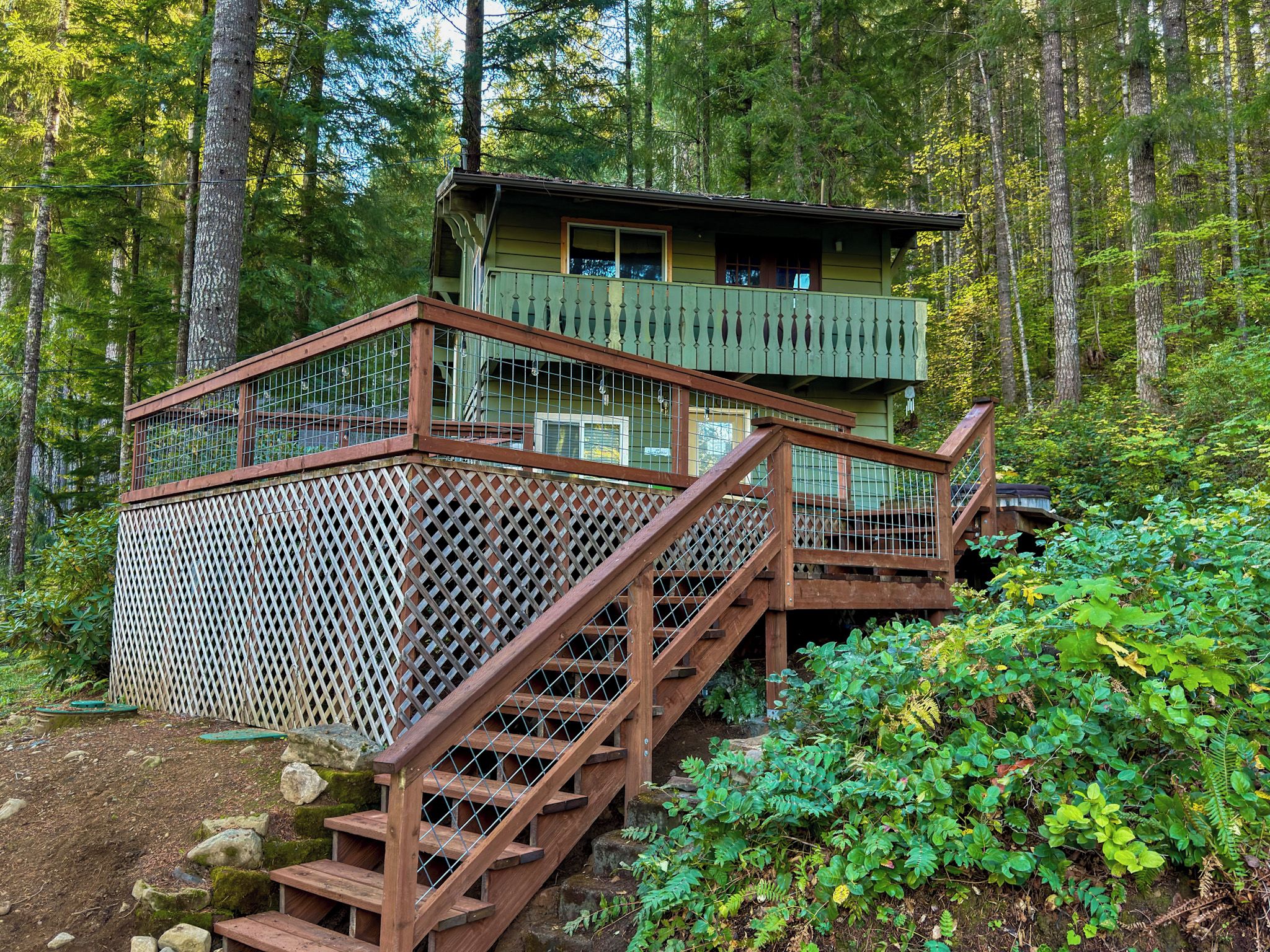 A wooden staircase leading to a cabin with a balcony, surrounded by dense forest.