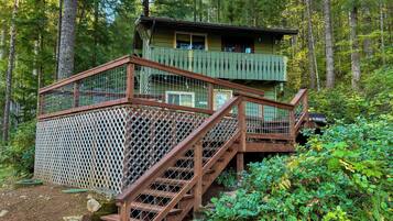 A wooden staircase leading to a cabin with a balcony, surrounded by dense forest.
