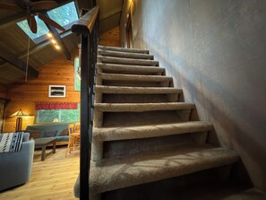 Un intérieur en bois avec un escalier recouvert de moquette, un canapé, une table et une lampe.
