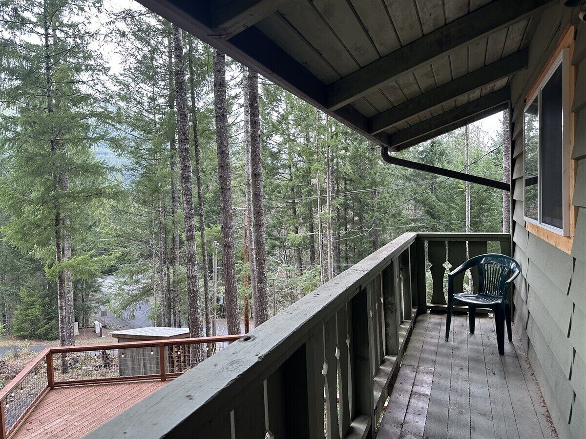 A wooden deck with a railing, a chair, and a table overlooking a forested area.