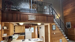 Et sommerhusinteriør med et tekøkken, trævægge, en trappe og et skilt med teksten 'LIFE IS BETTER CABIN'.