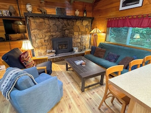 A cozy cabin interior with a stone fireplace, a sofa set, a coffee table, and a dining table. - Culps Cascade | Wi-Fi, Woodstove, Cedar Hot tub (Packwood)