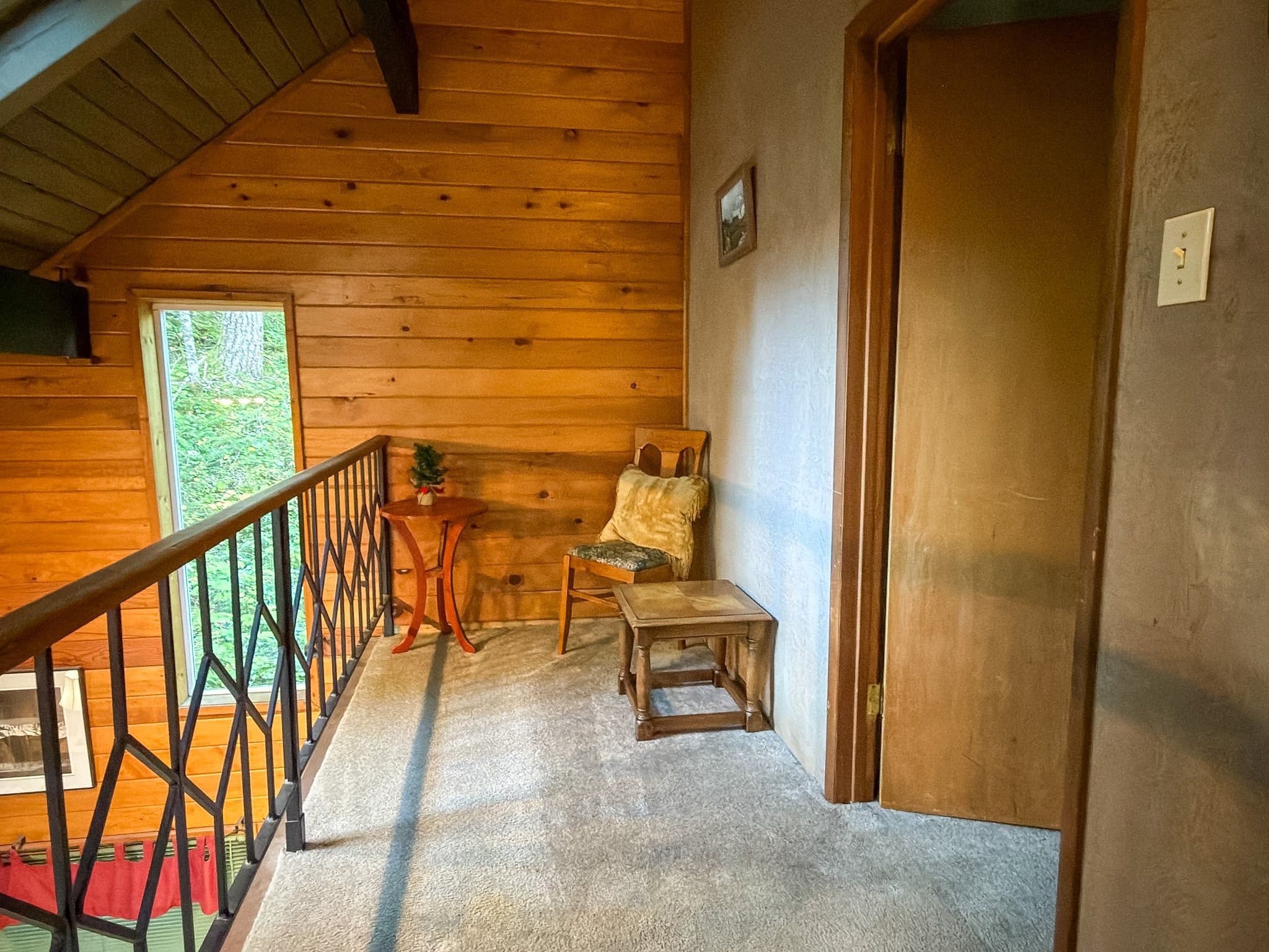 A wooden cabin interior with a staircase, a small table, a chair, and a door.