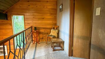 A wooden cabin interior with a staircase, a small table, a chair, and a door.