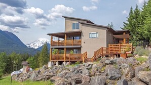 Eine zweistöckige Lodge mit Balkon, Holzgeländern und Blick auf schneebedeckte Berge.