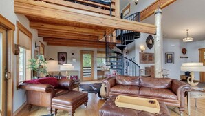 Ein geräumiges Wohnzimmer mit hoher Decke, einer Treppe und einem großen, braunen Ledersofa.