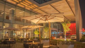 An outdoor dining area with tables and chairs, umbrellas, and potted plants. - Hilton Garden Inn Kuwait (Kuwait City)