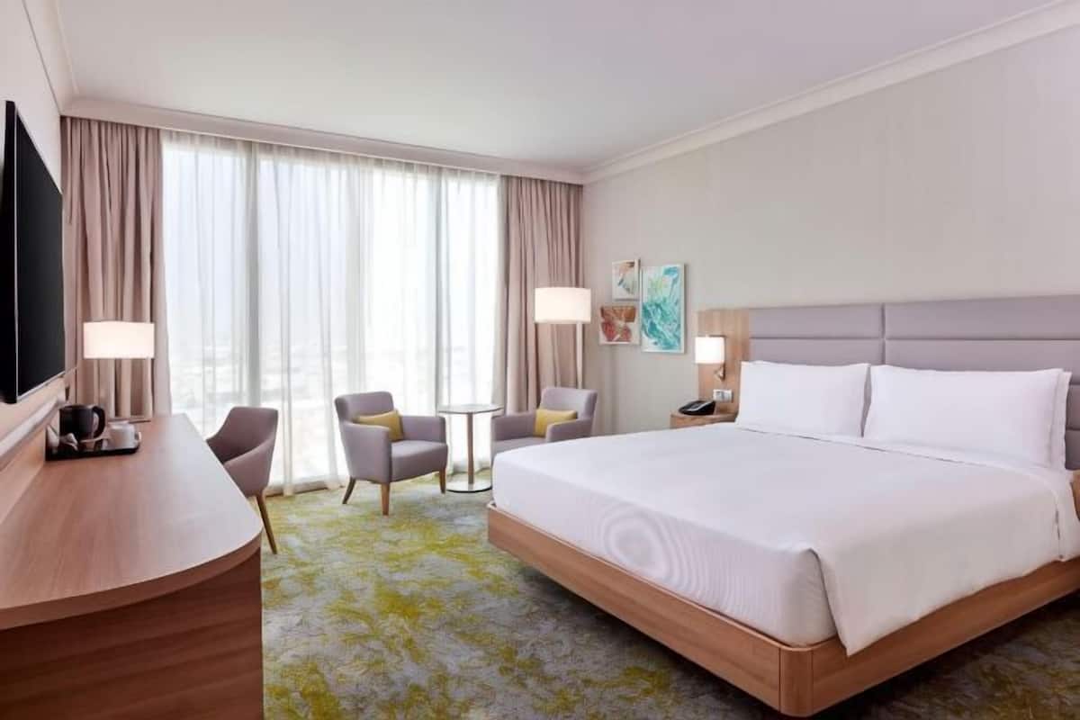 A hotel room with a large bed, two bedside tables, a desk, a chair, a small table, and a TV.