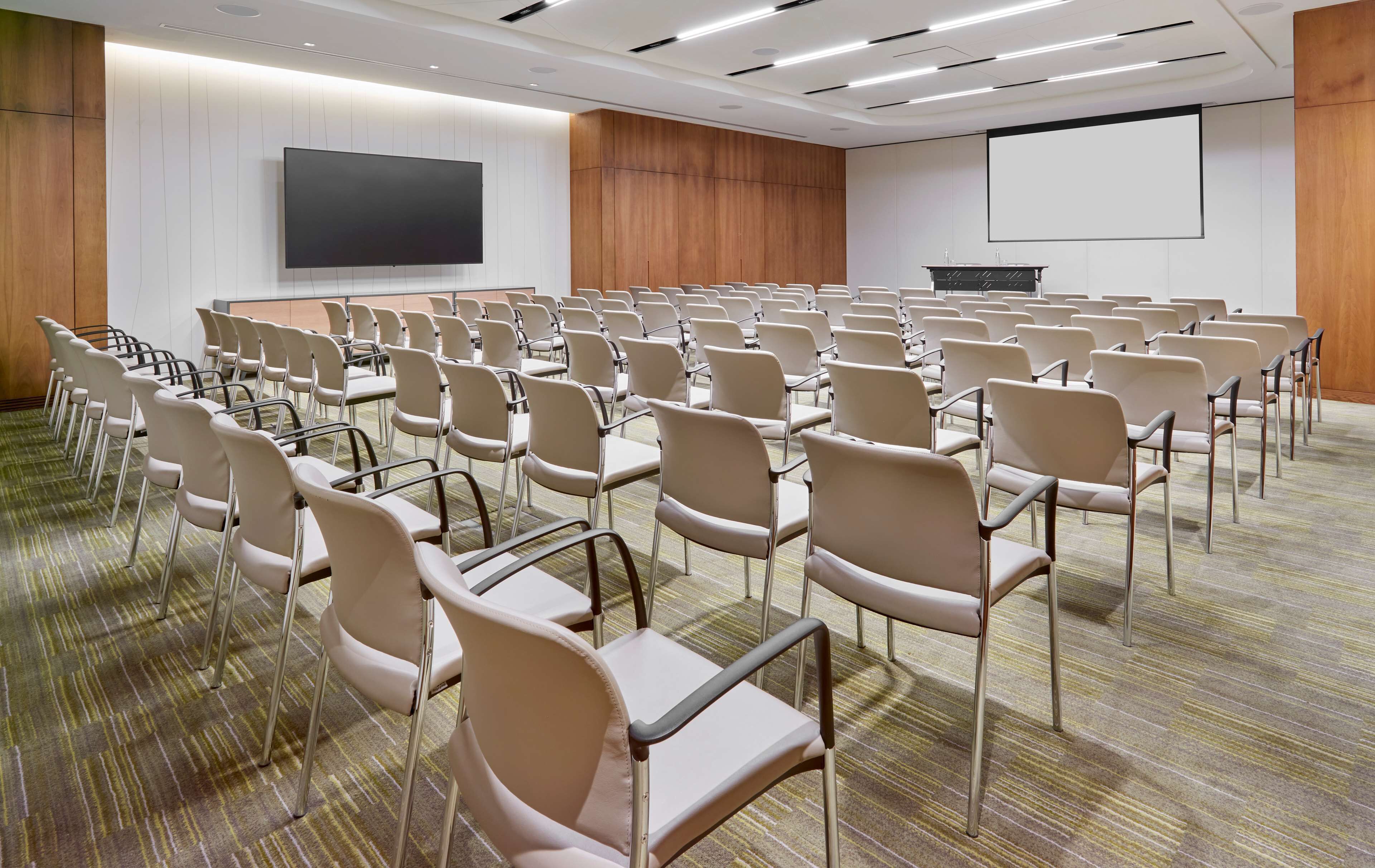 A conference room with rows of chairs, a large screen, and a podium.
