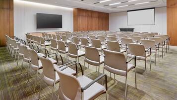 A conference room with rows of chairs, a large screen, and a podium.