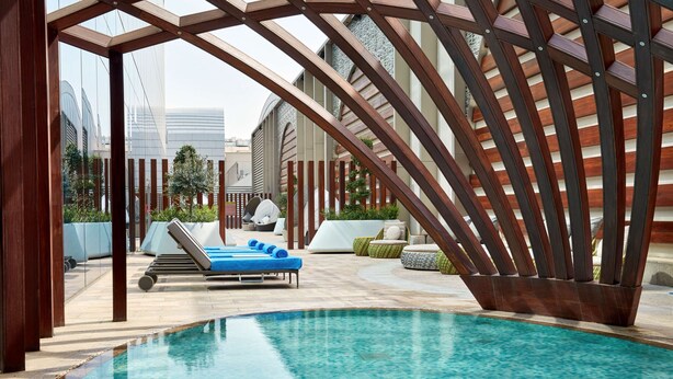 A modern pool area with a clear blue pool, lounge chairs, and a wooden pergola structure. - Hilton Garden Inn Kuwait (Kuwait City)
