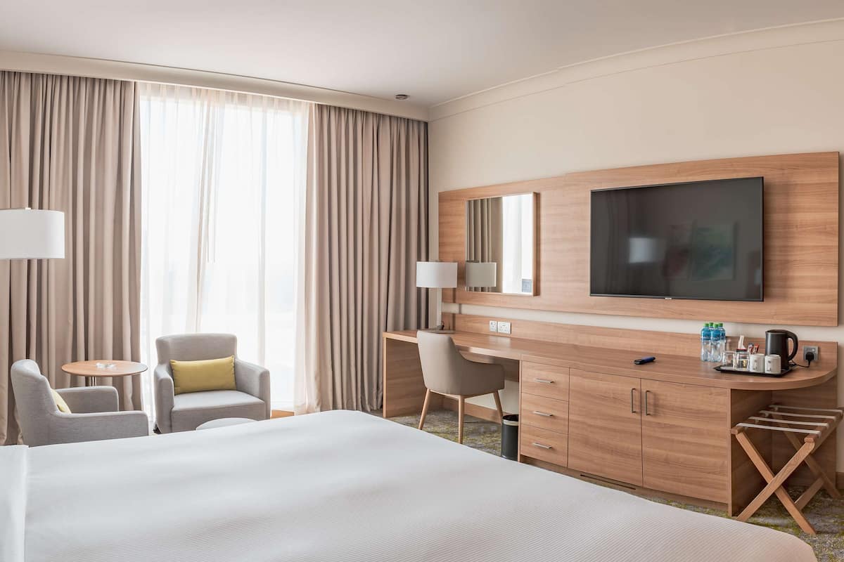 A hotel room with a large bed, a desk with a chair, a TV, and a wardrobe.
