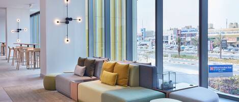 Un moderno vestíbulo de hotel con un amplio espacio de descanso, vistas a la ciudad y un cartel de Hilton Garden Inn.