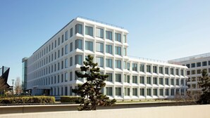 Un edificio moderno de varios pisos con fachada de líneas geométricas, grandes ventanales y techo plano.