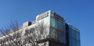 Un hotel Hilton Garden Inn con una fachada moderna de vidrio y un cielo azul despejado al fondo.