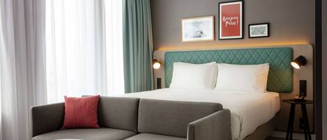 Una habitación de hotel con cama, sofá, una mesita y dos lámparas de pared.