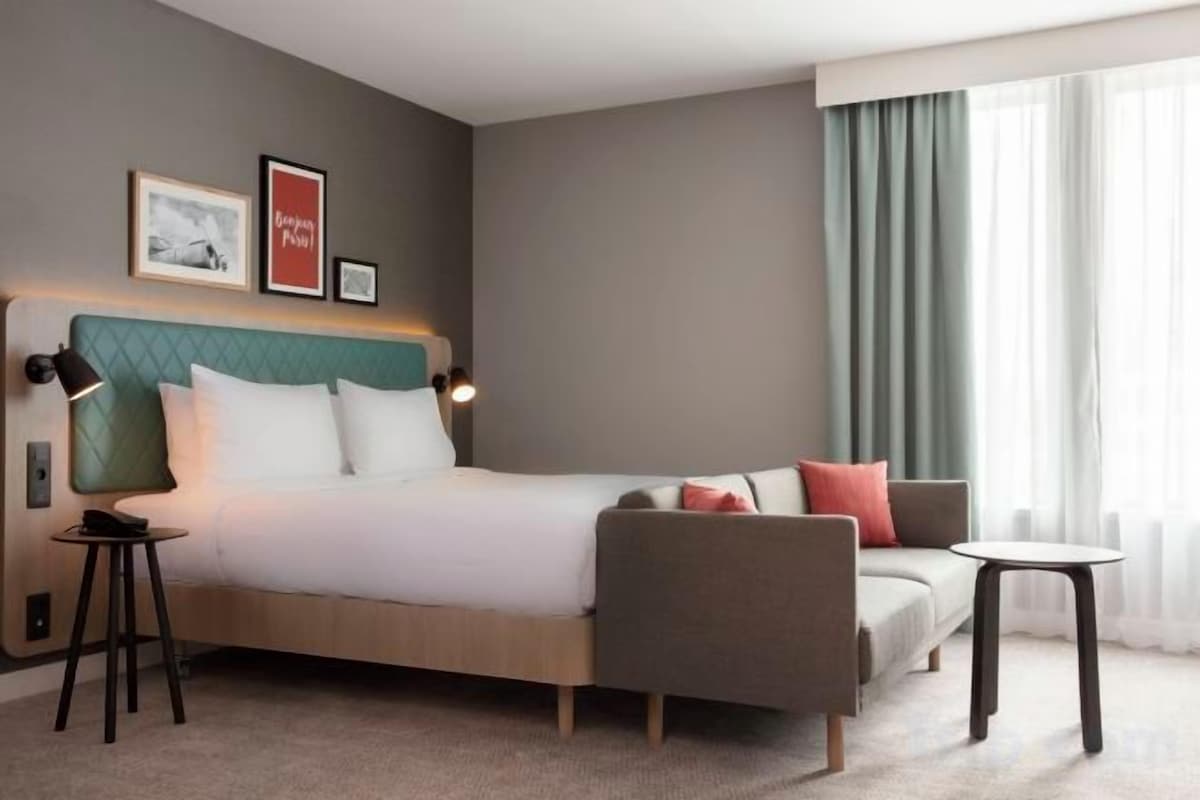 A hotel room with a bed, a sofa, a small table, and a window with curtains.