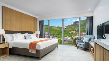 Une chambre d’hôtel moderne, dotée d’un grand lit, d’un bureau et offrant une vue sur une colline verdoyante.