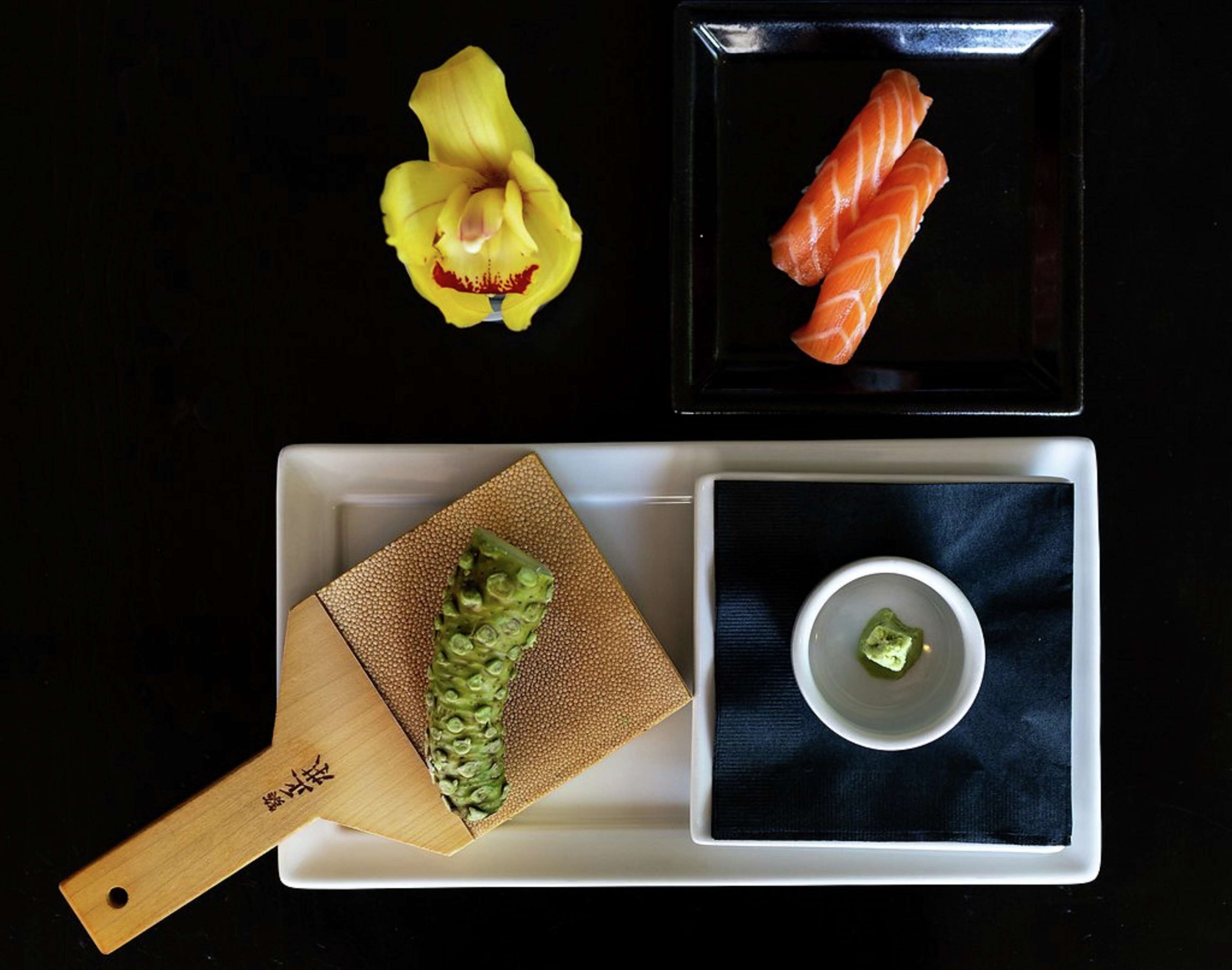 Una bandeja con sushi, un vegetal verde y una flor.
