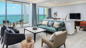 A modern living room with a large window overlooking the sea, a sofa set, a coffee table, and a TV. - Koi Resort Saint Kitts, Curio Collection by Hilton (Basseterre)