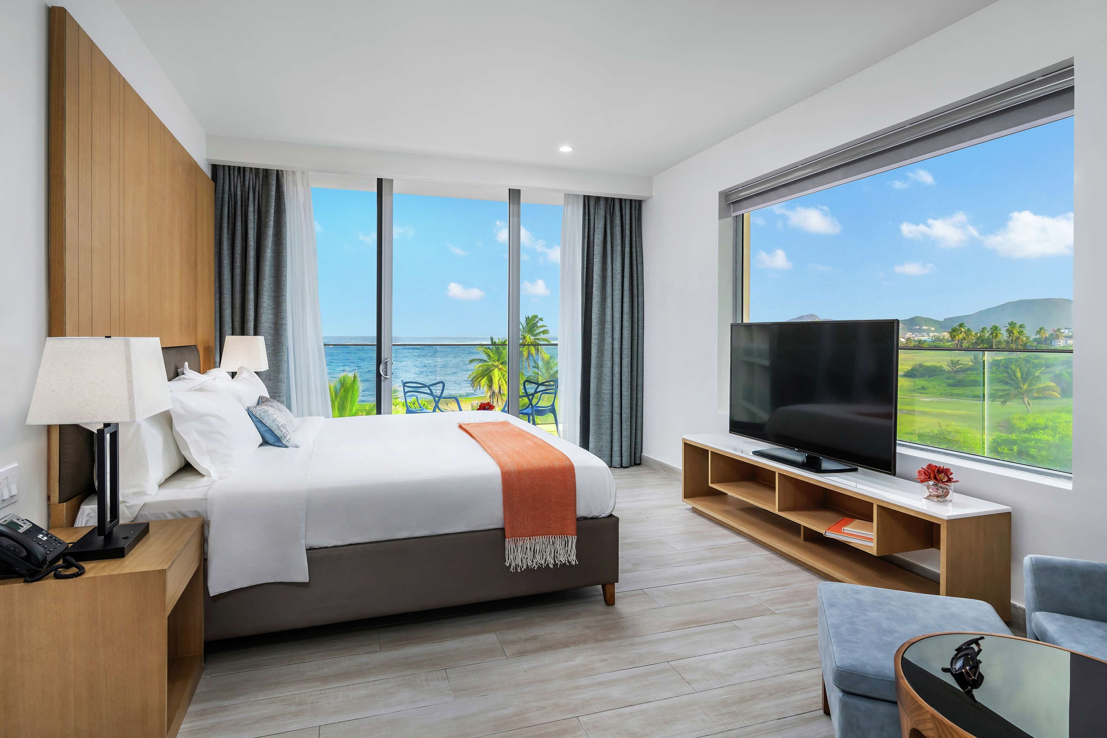Una habitación de hotel moderna con una cama grande, televisión y balcón con vista al océano.