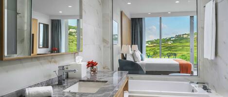 A modern bathroom with a large mirror, a marble sink, a bathtub, and a view of a green landscape through large windows.