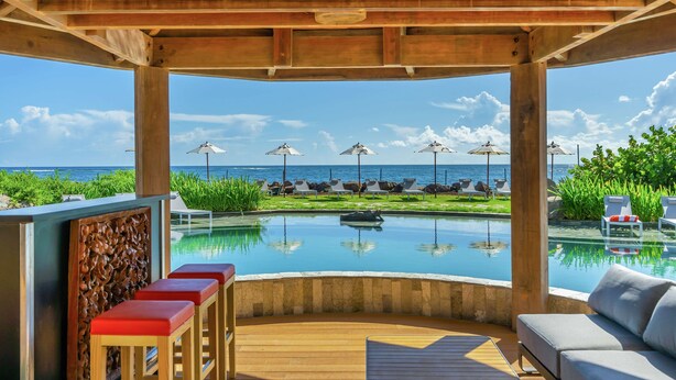A wooden deck with a pool, lounge chairs, and a view of the ocean. - Koi Resort Saint Kitts, Curio Collection by Hilton (Basseterre)